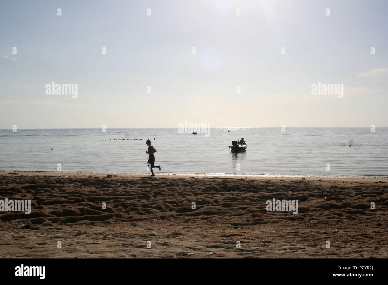 Uomo che corre sulla Thailandia Beach, con piccola barca in background Foto Stock