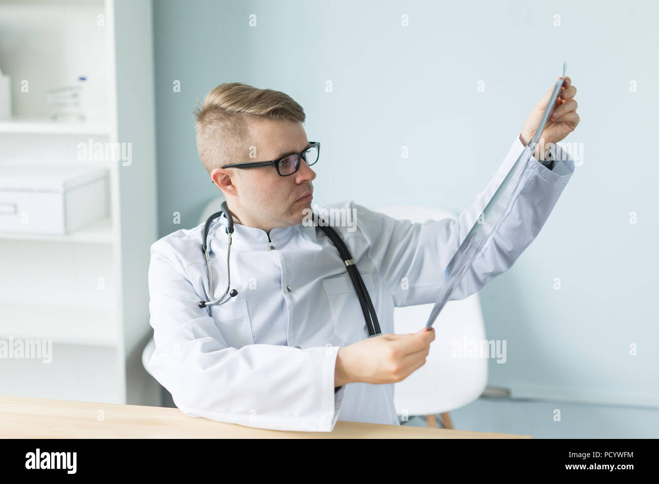 Giovane medico caucasica seduta nel suo ufficio e alla ricerca di immagini a raggi X Foto Stock