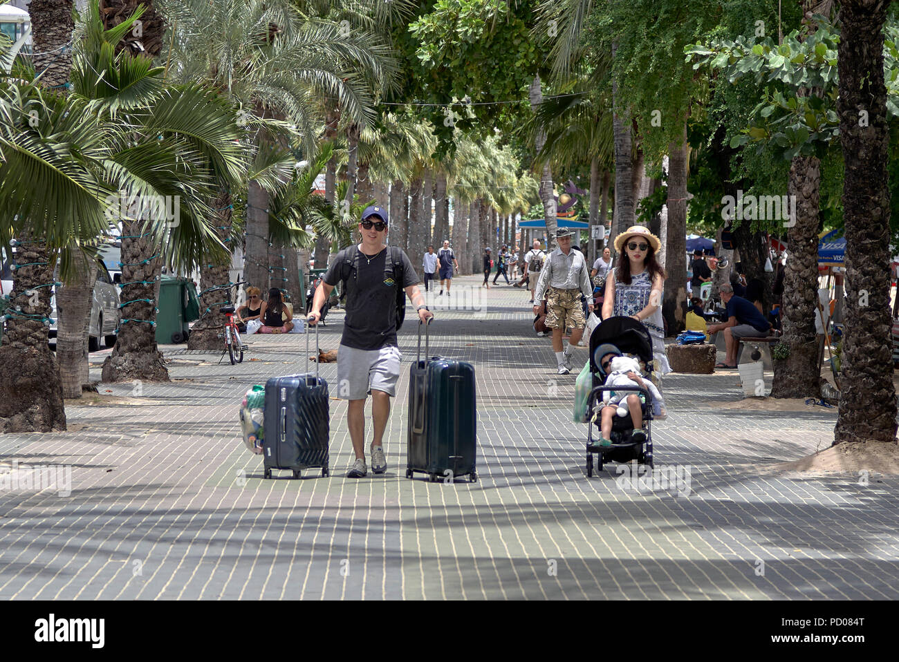 Giovane famiglia in vacanza a piedi lungo la strada con le valigie e il bambino nel passeggino Foto Stock
