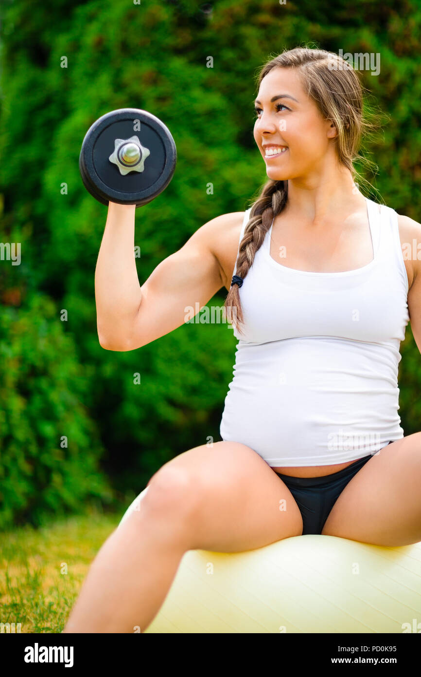 Donna incinta sorridente durante il sollevamento di pesi sulla sfera di Yoga Foto Stock