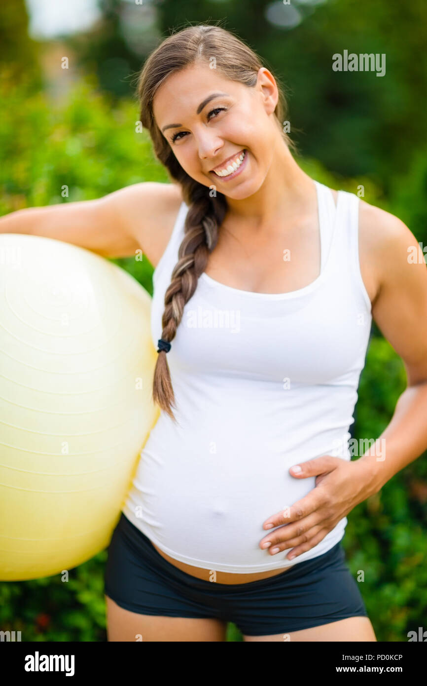 Sorridente Donna Incinta toccando ventre tenendo esercizio Bal Foto Stock