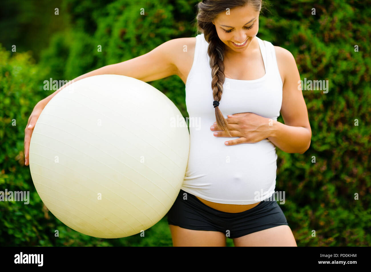 Donna incinta toccando ventre tenendo palla Fitness in posizione di parcheggio Foto Stock