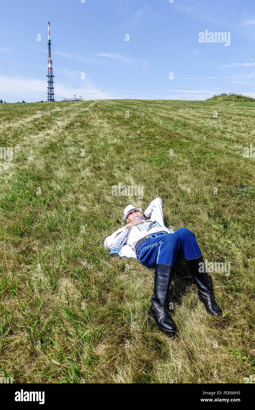 Uomo in costumi folk giacente sul prato di montagna, Velka Javorina, Slovacchia Foto Stock