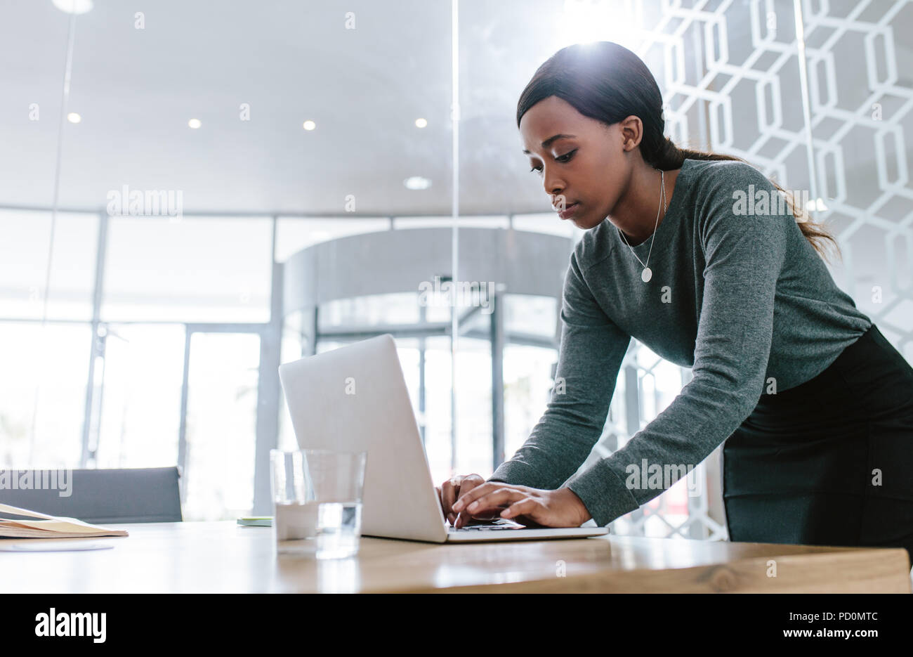 Giovane donna in piedi da tavolo da conferenza e di lavoro sul computer portatile. Femmina di preparare una proposta di business prima di una riunione nella sala riunioni. Foto Stock