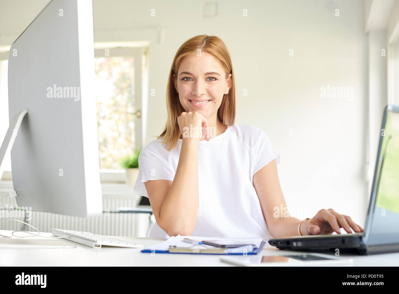 Colpo di sorridente giovane imprenditrice usando il suo computer portatile mentre è seduto alla scrivania in ufficio e di lavoro on-line. Foto Stock