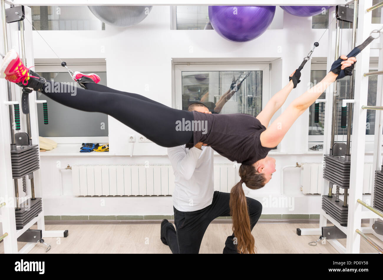 Donna stretching sul cavo crossover macchina con istruttore di palestra Foto Stock