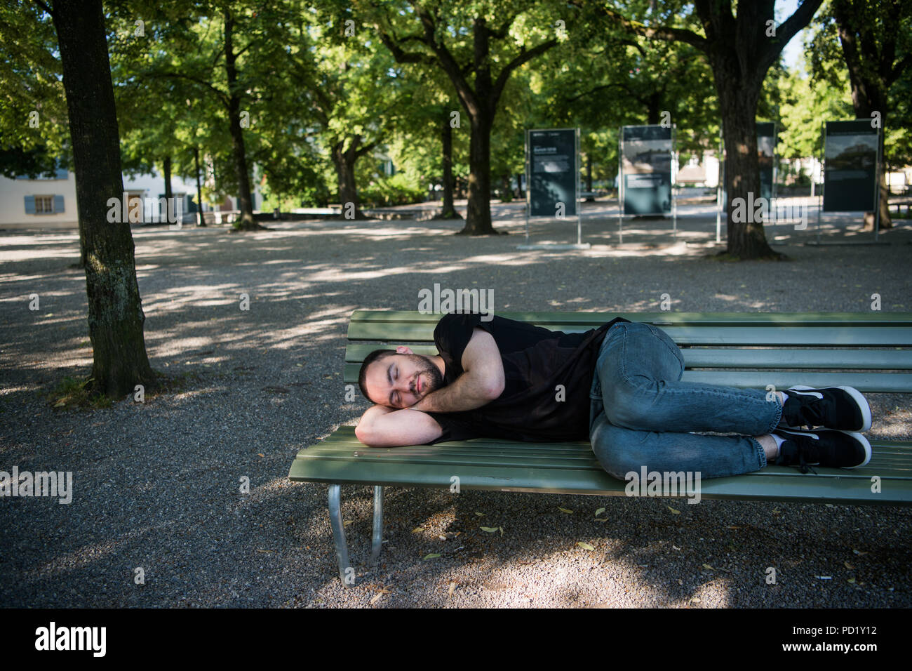 Poveri senzatetto uomo dorme sul banco di legno in posizione di parcheggio Foto Stock