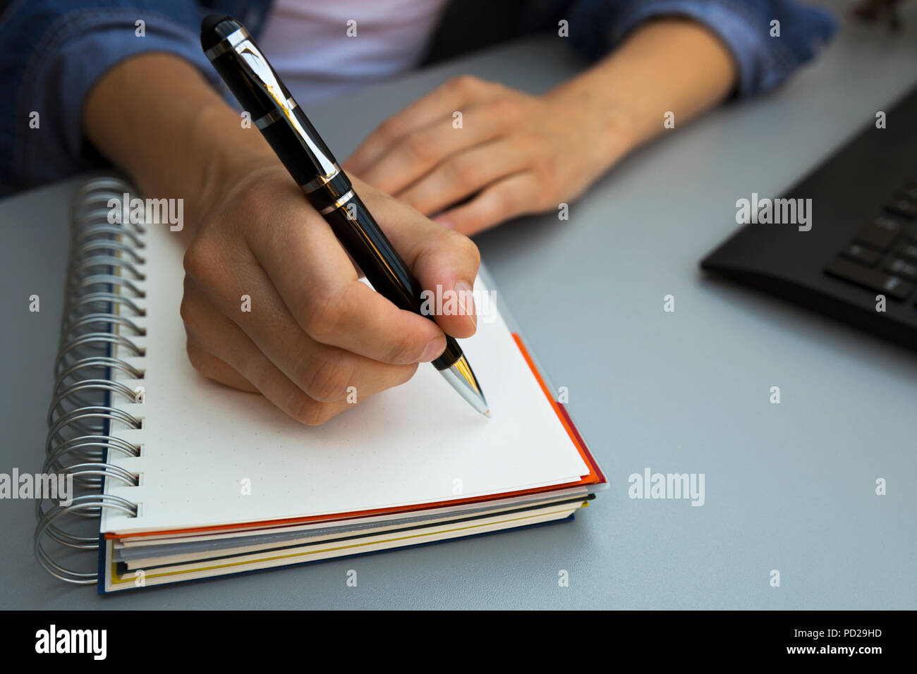 Donna con le mani la scrittura della penna sul notebook. Moderno edificio grigio scrivania in ufficio. Lavorando, concetto di scrittura Foto Stock