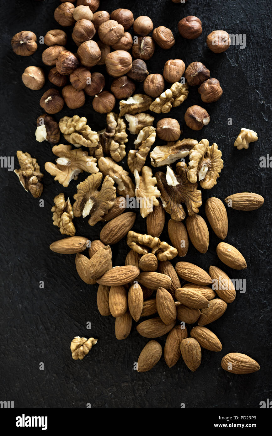 I dadi di organico. Vari dadi (noci, nocciole, mandorle) sulla pietra nera di sfondo, vista dall'alto, copia dello spazio. Foto Stock