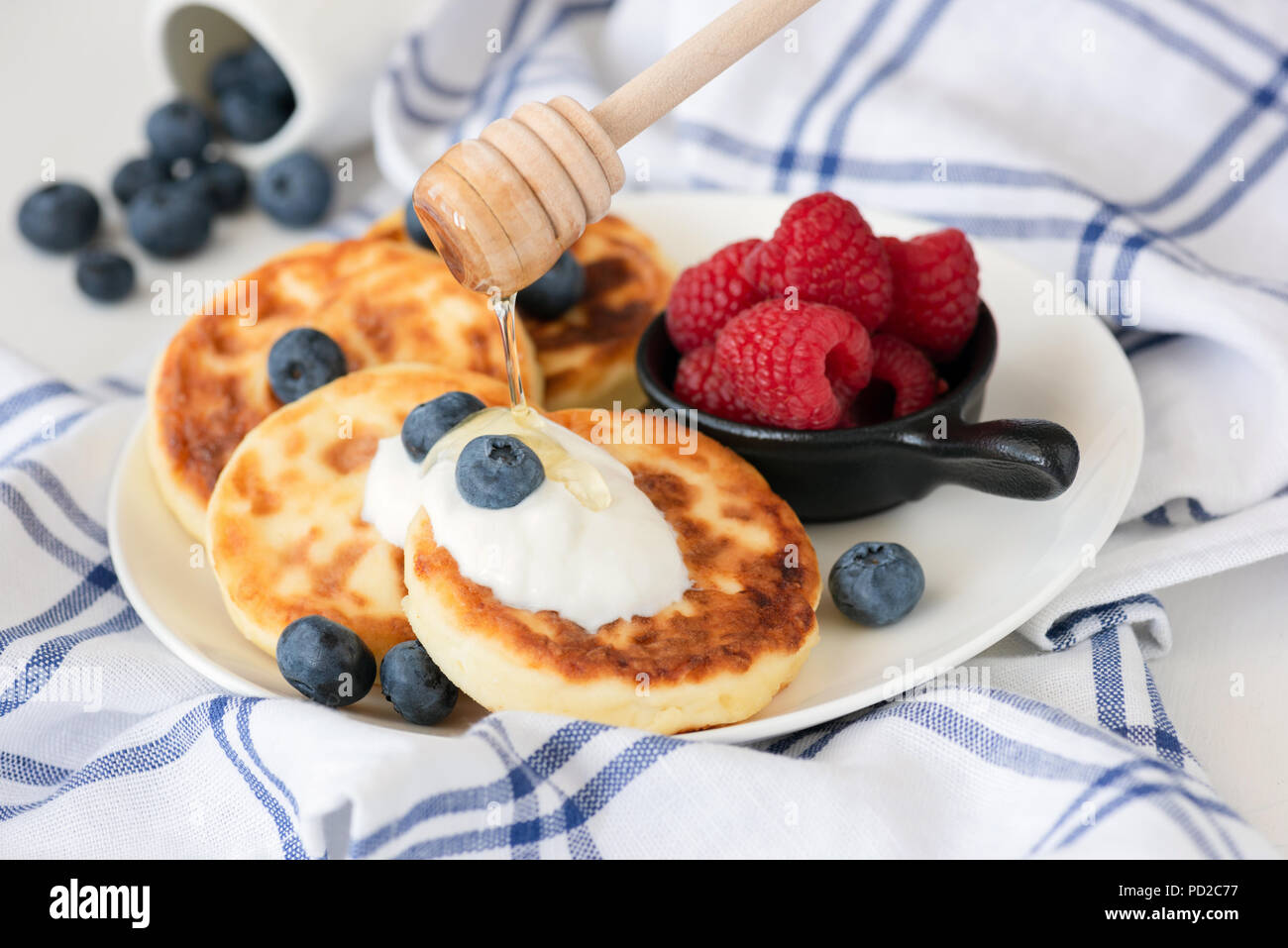 Cottage cheese frittelle o sirniki con panna acida, miele e frutti di bosco. Vista ingrandita, il fuoco selettivo. Cucina russa Foto Stock