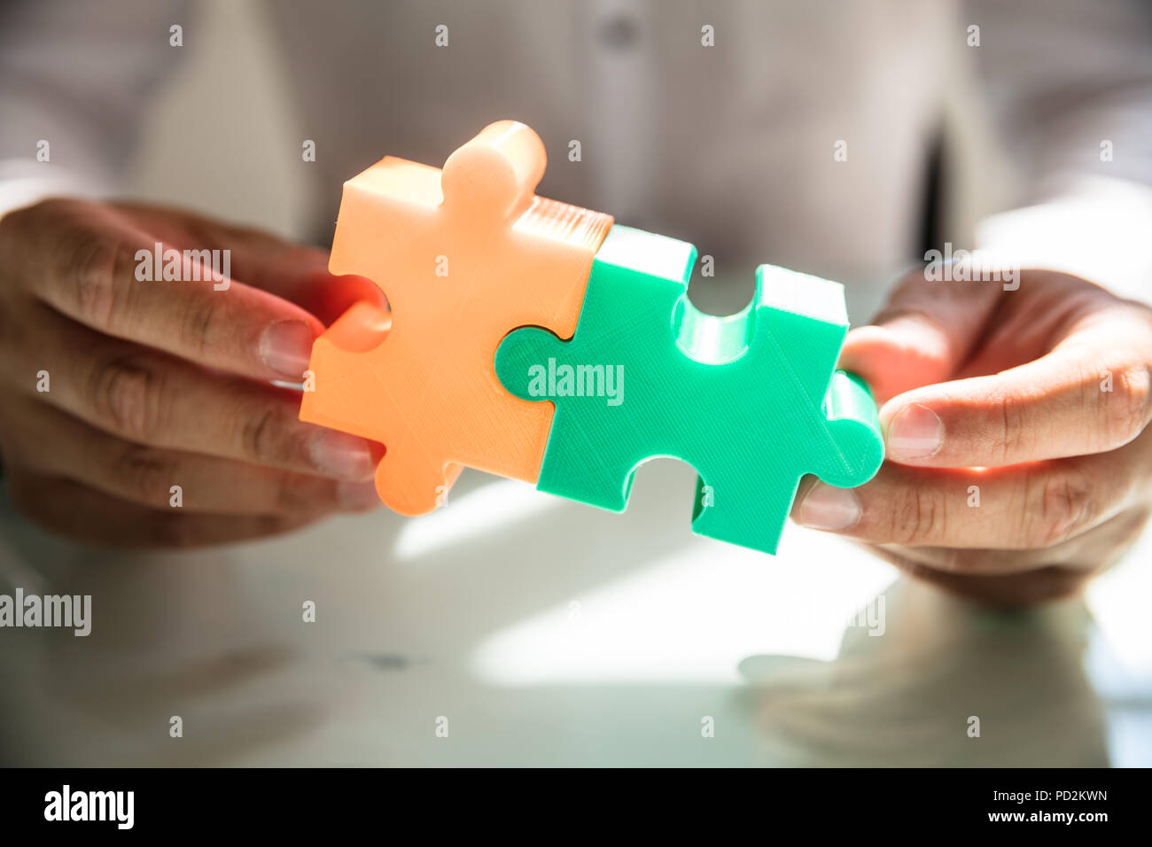 Imprenditore il lato di collegamento di due coloratissimi jigsaw puzzle in ufficio Foto Stock