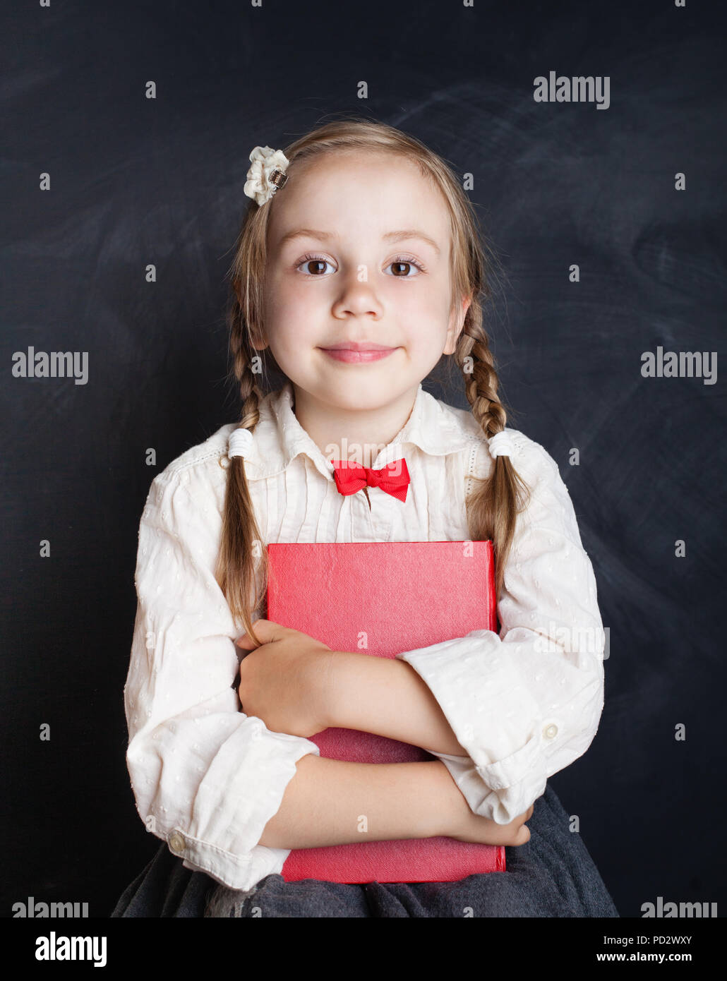 Сhild ragazza in uniforme scolastica vestiti con libro su chalk board sfondo (bambino 5-6 anni). Si torna a scuola, la scuola elementare e istruzione concep Foto Stock