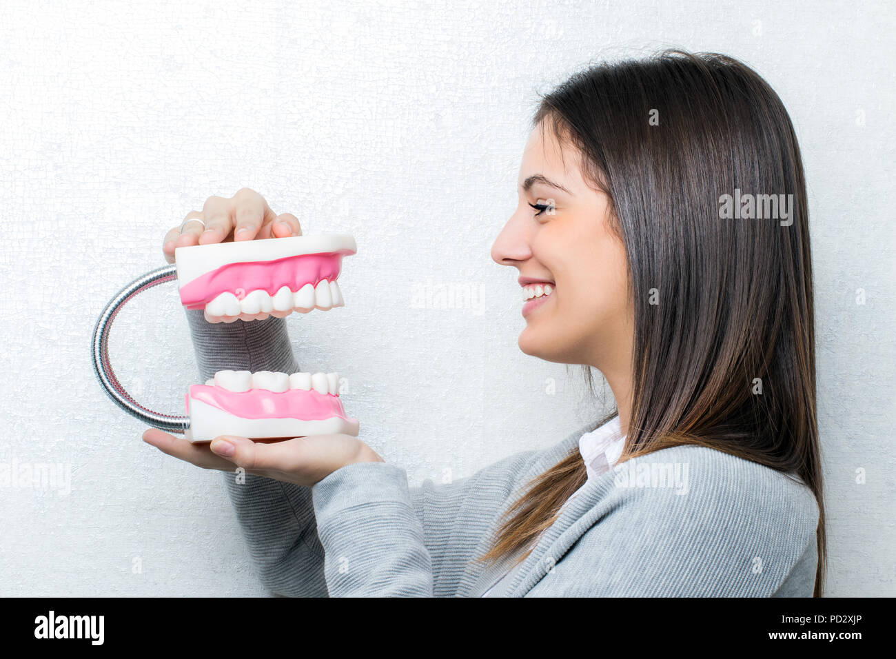 Close up ritratto di attraente ragazza giovane azienda sovradimensionata denti umani protesi.Vista laterale della donna contro la luce sullo sfondo a trama. Foto Stock