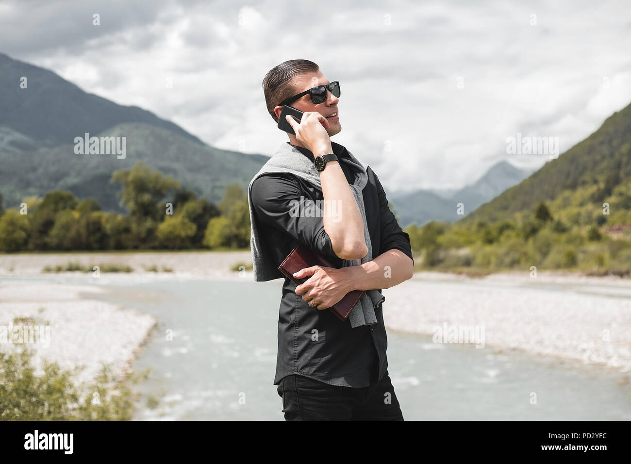 Imprenditore in mountain riverside rendendo chiamata dello smartphone, Francenigo, Veneto, Italia Foto Stock