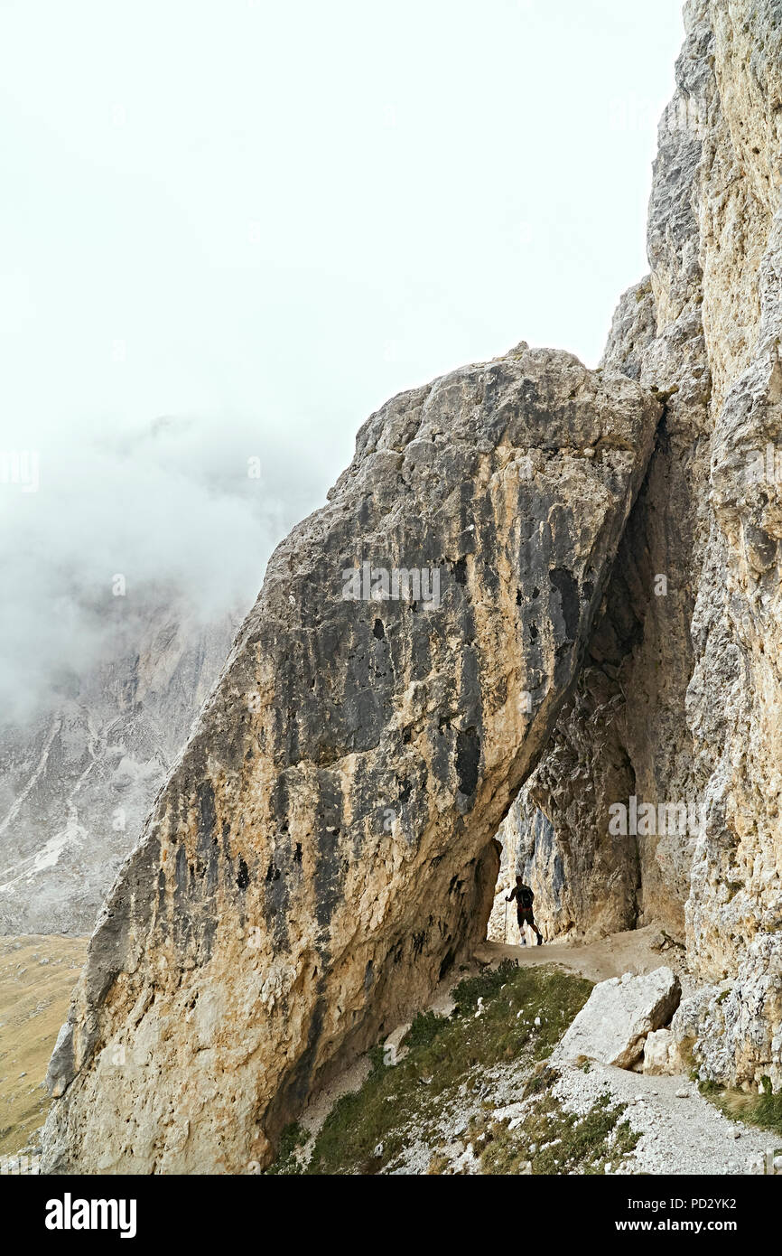 Escursionista passando sotto l'arco in pietra, Canazei, Trentino-Alto Adige, Italia Foto Stock
