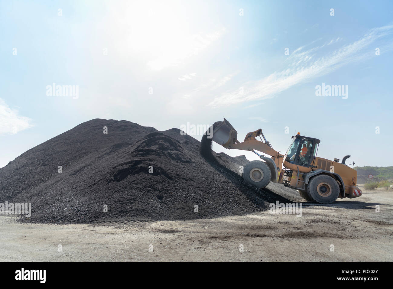Escavatore con un grande mucchio di suolo riciclato in calcestruzzo sito di riciclaggio Foto Stock