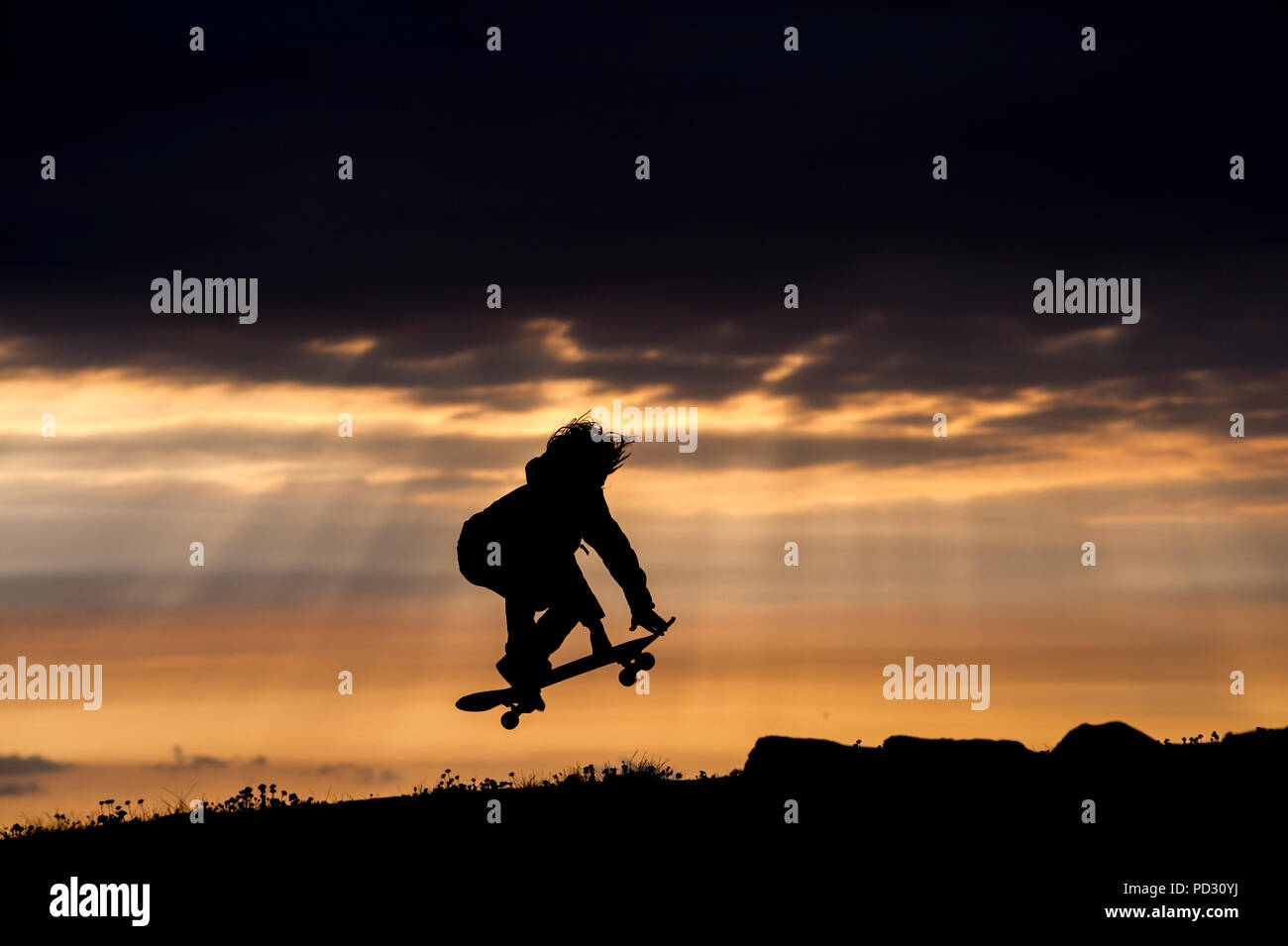 Ragazzo giovane lo skateboard al tramonto, saltando, a metà in aria, Doolin, Clare, Irlanda Foto Stock
