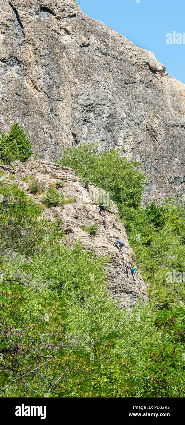 Una famiglia inglese in vacanza a L'Argentierre la Bessee, Francia, salire la via ferrrata sulla ripida scogliera di roccia di fronte alla torre dell orologio. Foto Stock