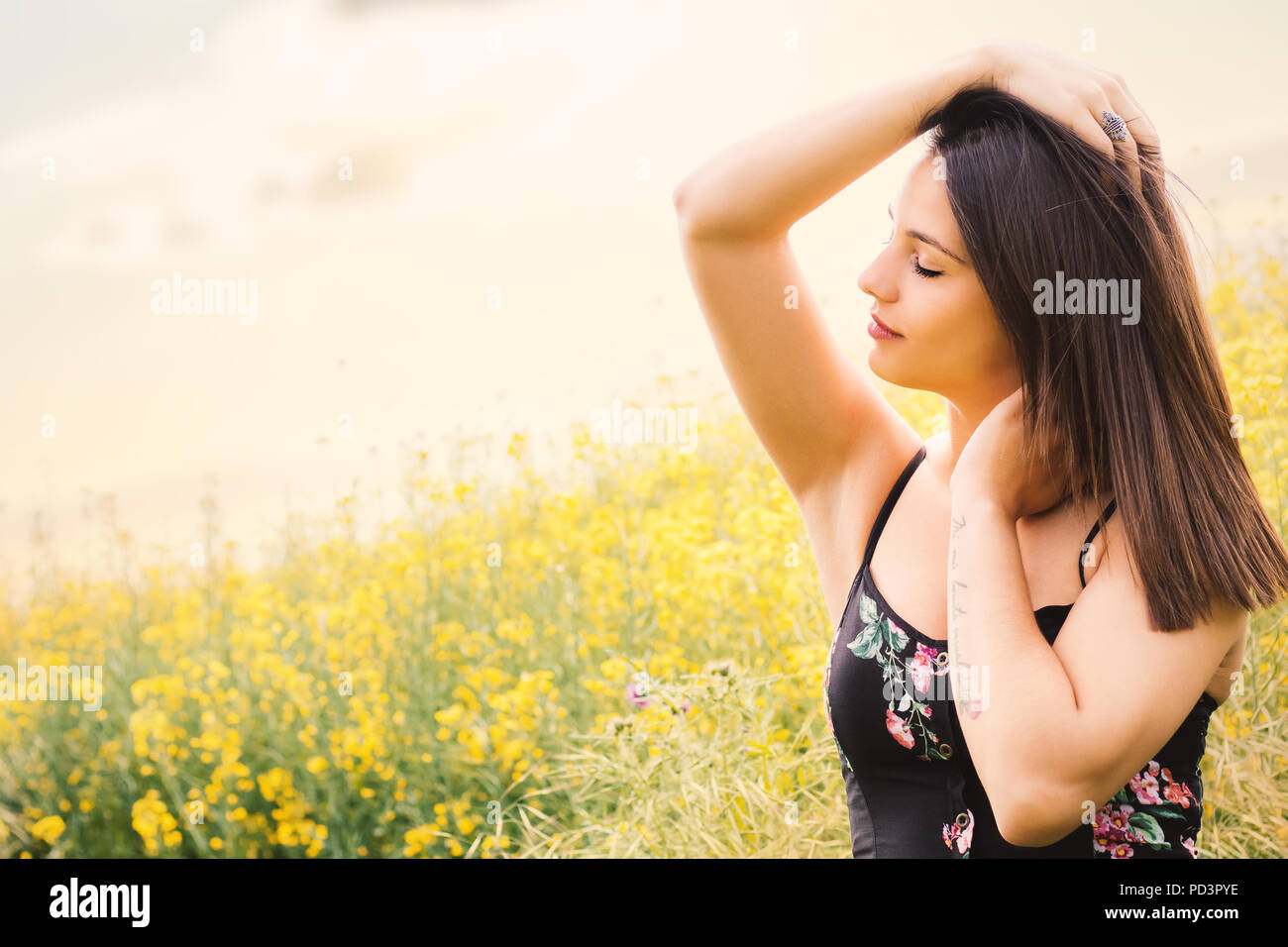 Close up ritratto di donna attraente rilassante con gli occhi chiusi in fiore giallo campo. Foto Stock