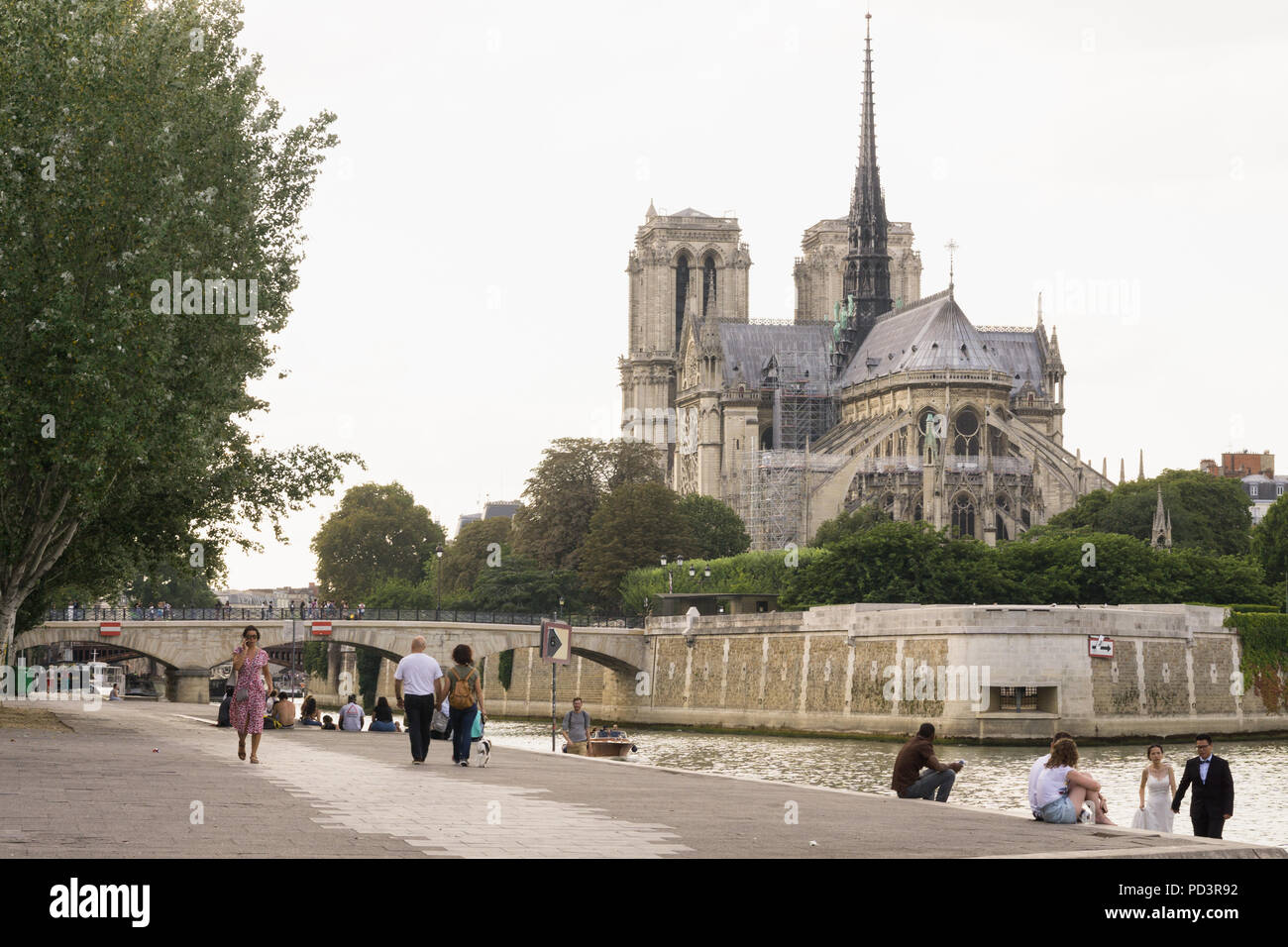 Parigi Notre Dame - la gente camminare lungo la Senna argine sinistro, la cattedrale di Notre Dame in background. Foto Stock
