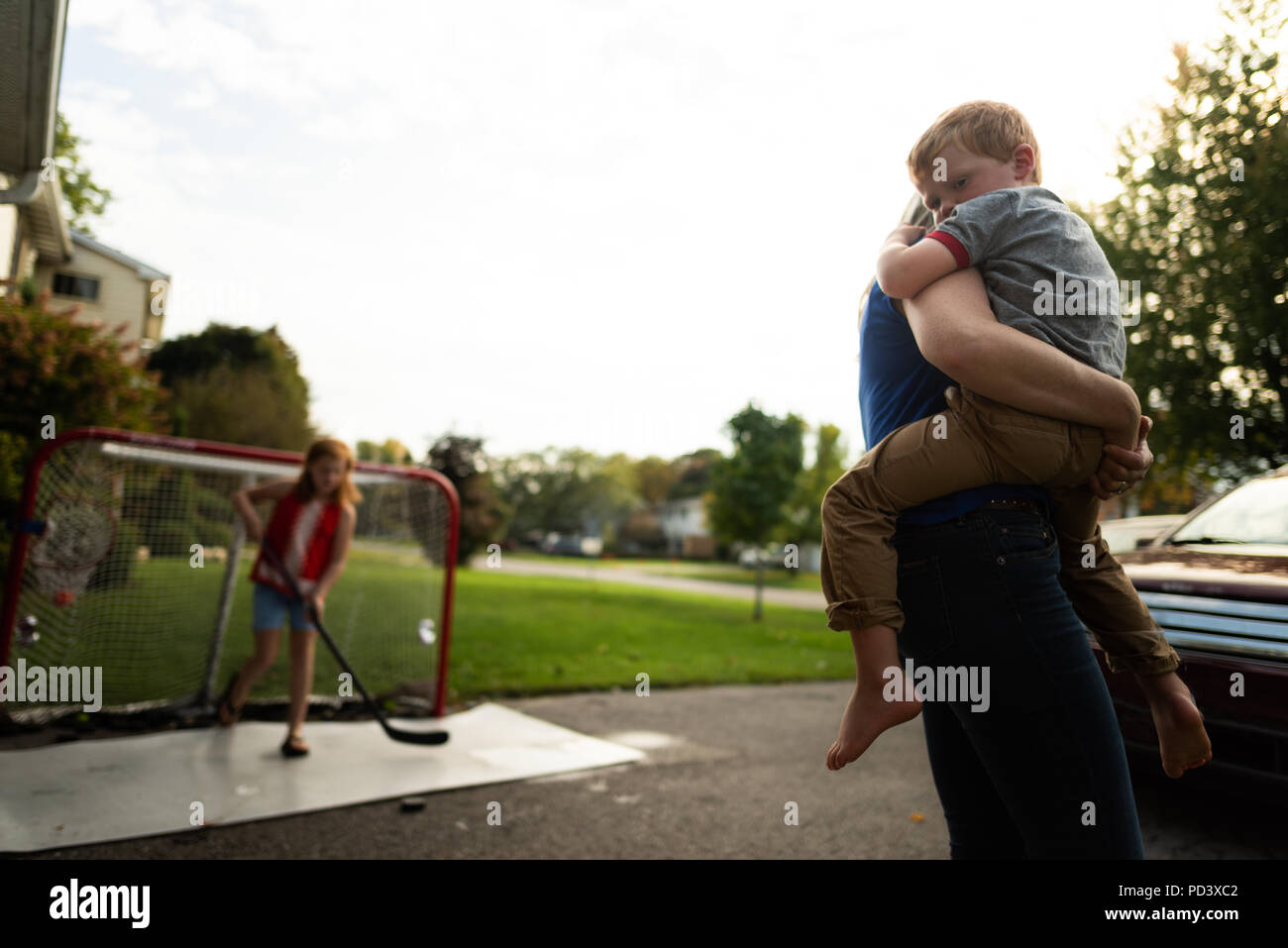 Adulto di portare il ragazzo, ragazza giocare ad hockey in background Foto Stock