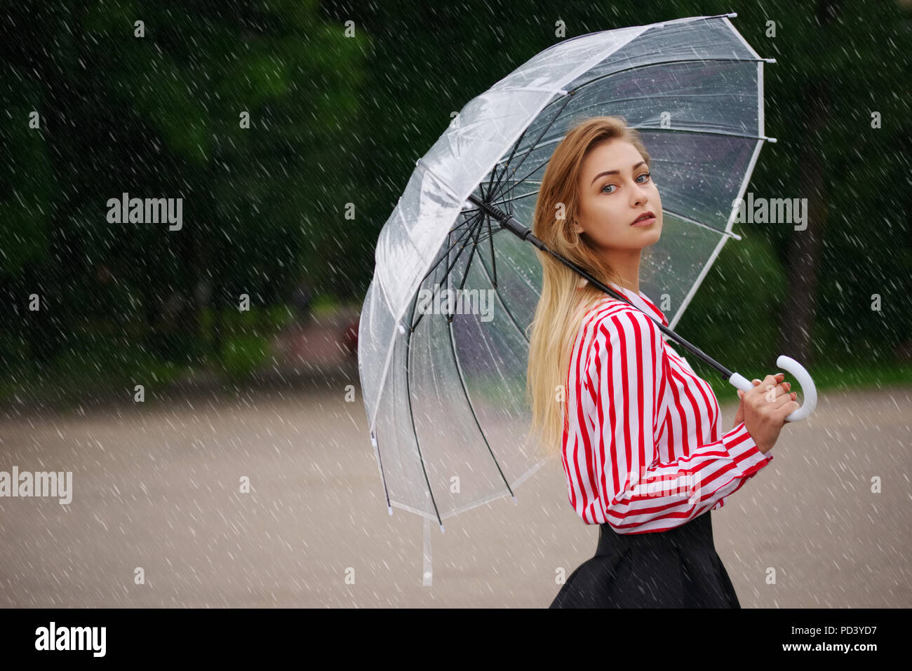Bellissima ragazza con ombrello trasparente in condizioni di tempo piovoso Foto Stock