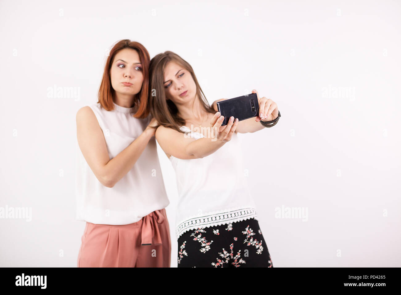 Due ragazze felici di prendere una selfie in studio su un muro bianco Foto Stock