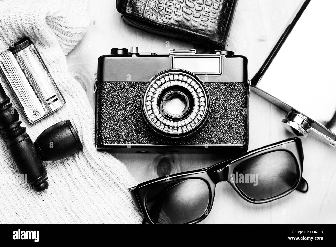 Gli accessori della persona creativa 35-mm fotocamera a pellicola, misuratore di esposizione nella custodia di pelle, pallone di acciaio, occhiali da sole e il fumo impostato su sfondo di legno. Foto Stock