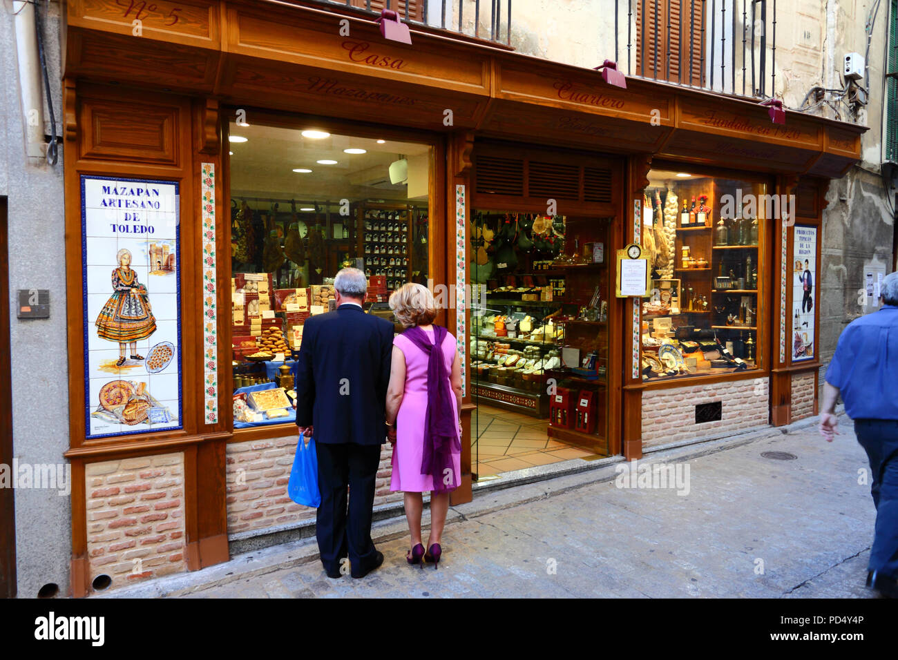 Marito e moglie ben vestiti che guardano dalla finestra del negozio che vende il famoso marzapane locale, Toledo, Castiglia-la Mancha, Spagna Foto Stock