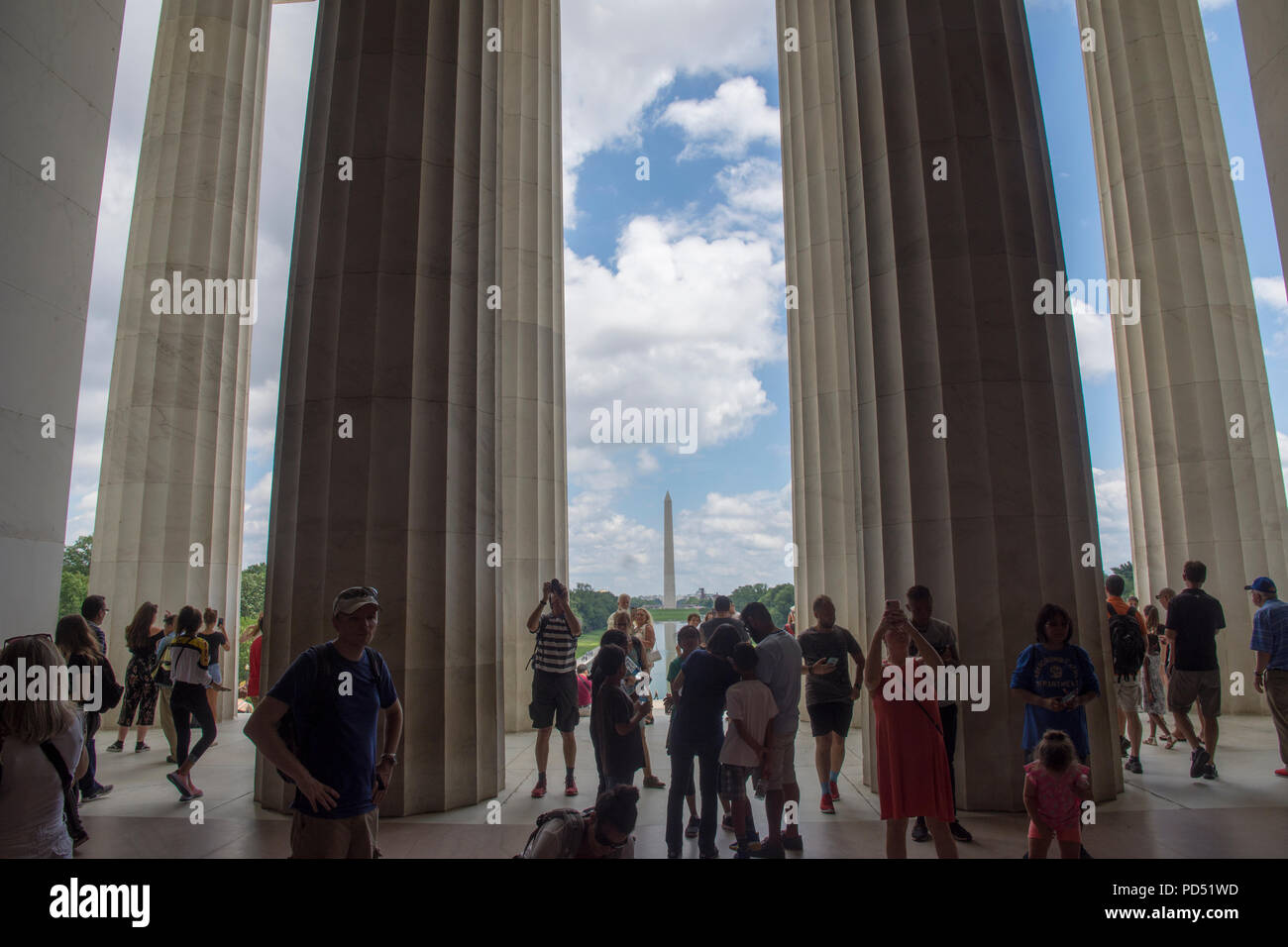 Alte colonne del Lincoln Memorial salire oltre i visitatori in un giorno d'estate. Il Monumento a Washington e il blu del cielo con il bianco puffy nuvole sono in background. Foto Stock