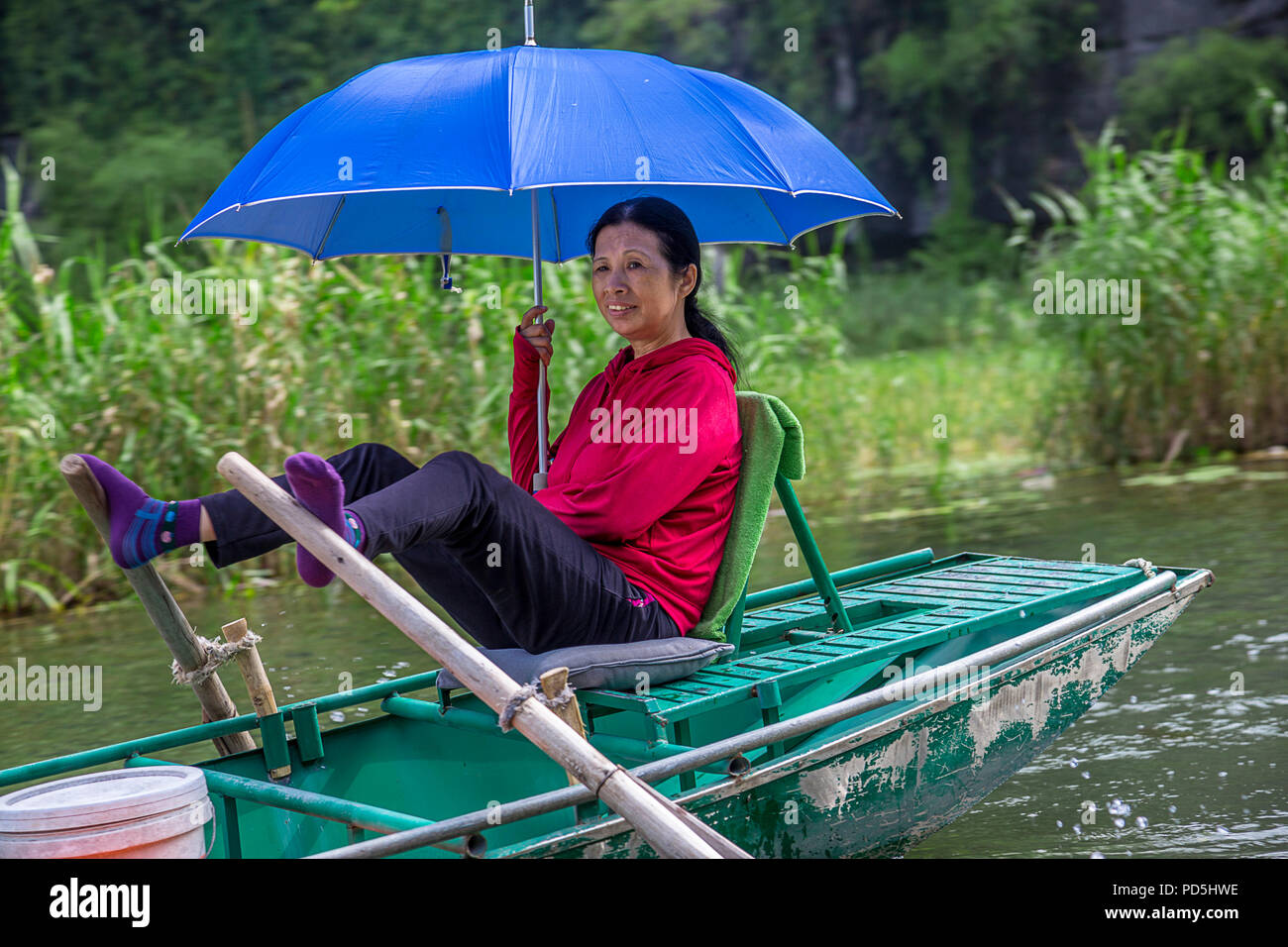 Asian lady con un blu umbrealla remare una barca con i suoi piedi. Editoriale: Tam Coc Ninh Binh 13 luglio 2017 Boatsman Foto Stock