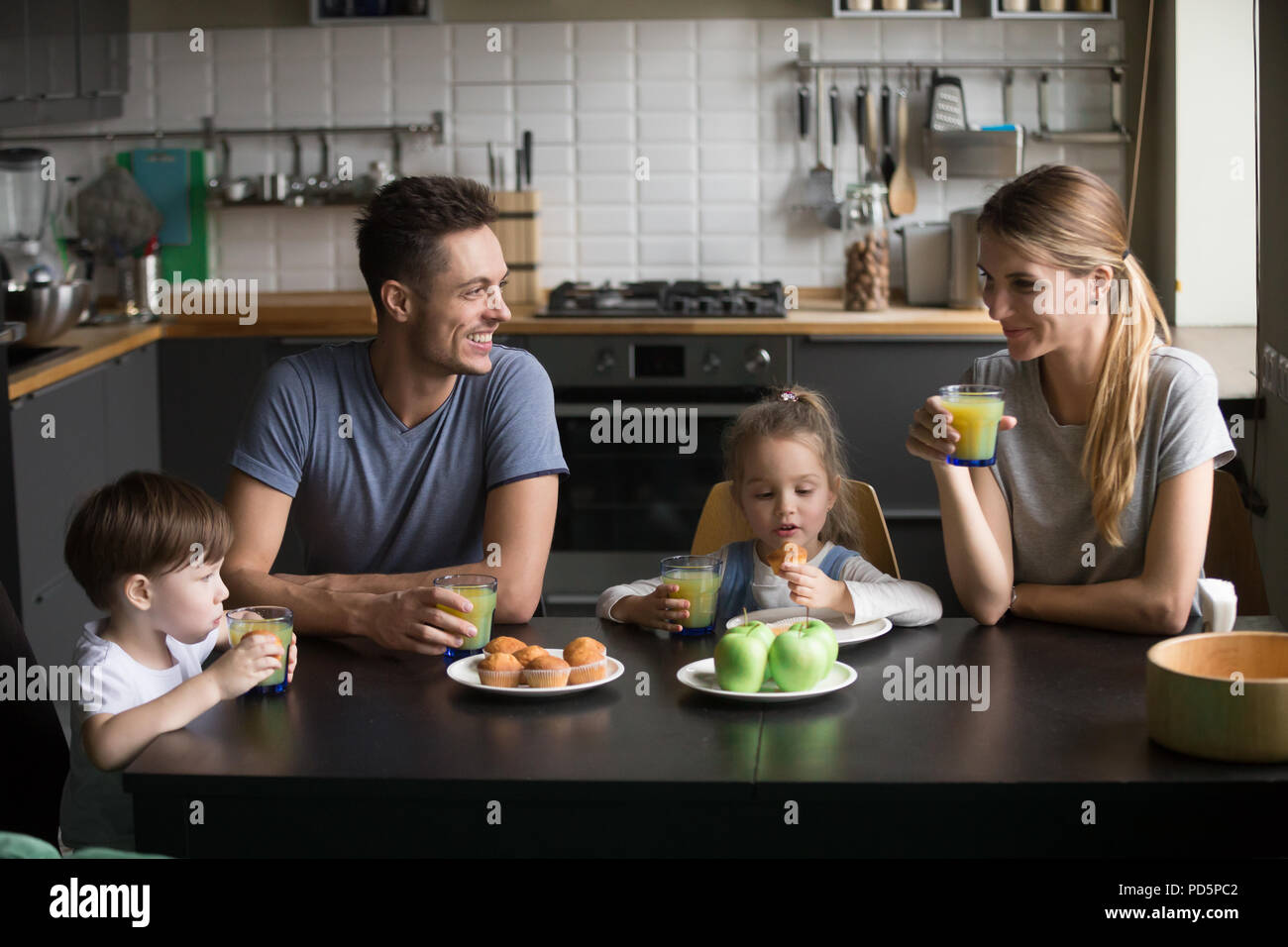 La famiglia felice e i bambini aventi la prima colazione seduti al tavolo della cucina Foto Stock