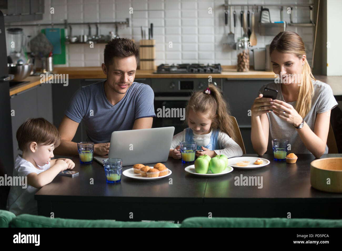 I genitori usando il laptop e smartphone avente la colazione del mattino wi Foto Stock