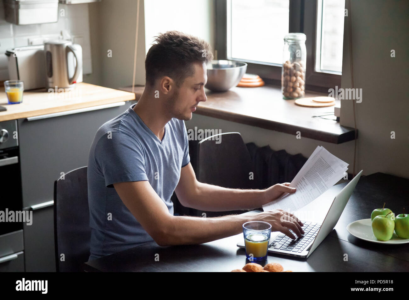 Giovane uomo che lavora con il computer portatile mentre si consuma la colazione a casa Foto Stock