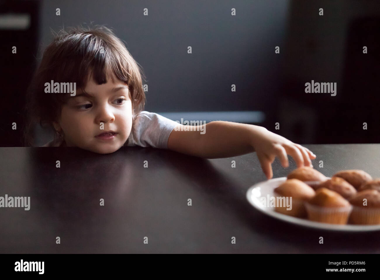 Astuzia carino bambina rubare deliziosi muffin su tavola Foto Stock