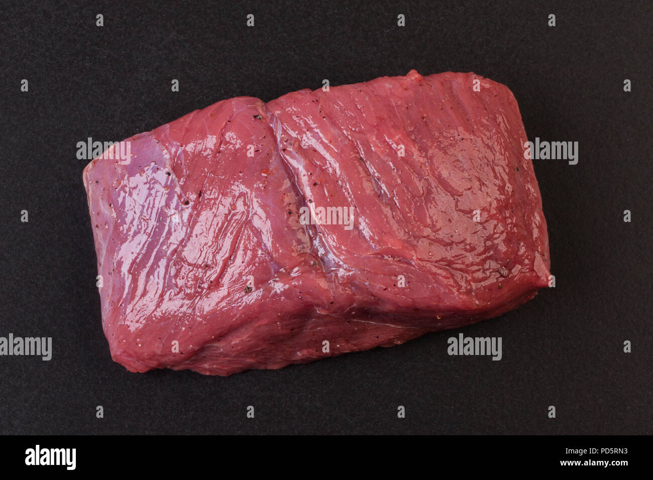 Un pezzo di carne cruda su una tavola nera Foto Stock