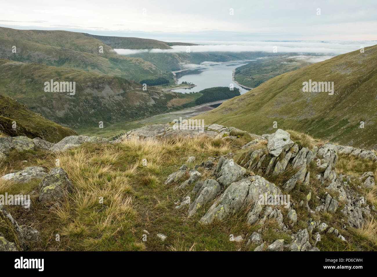 Vista da uno sperone roccioso su Harter cadde nel distretto del lago. Un basso Scafell serbatoio in distanza e basse nubi appeso a metà il fells Foto Stock