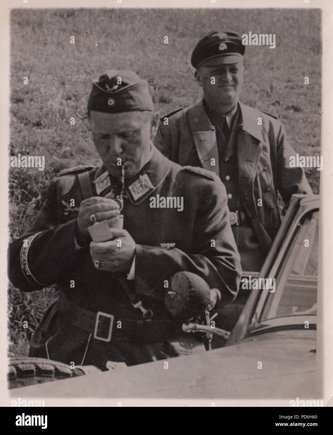 Immagine da l'album fotografico di Oberleutnant Oscar Müller di Kampfgeschwader 1: Durante una visita a II. Gruppe, Kampfgeschwader 1, Reichsmarschall Hermann Göring illumina il suo tubo, mentre il suo driver SS detiene la portiera della macchina. Estate 1940 Foto Stock