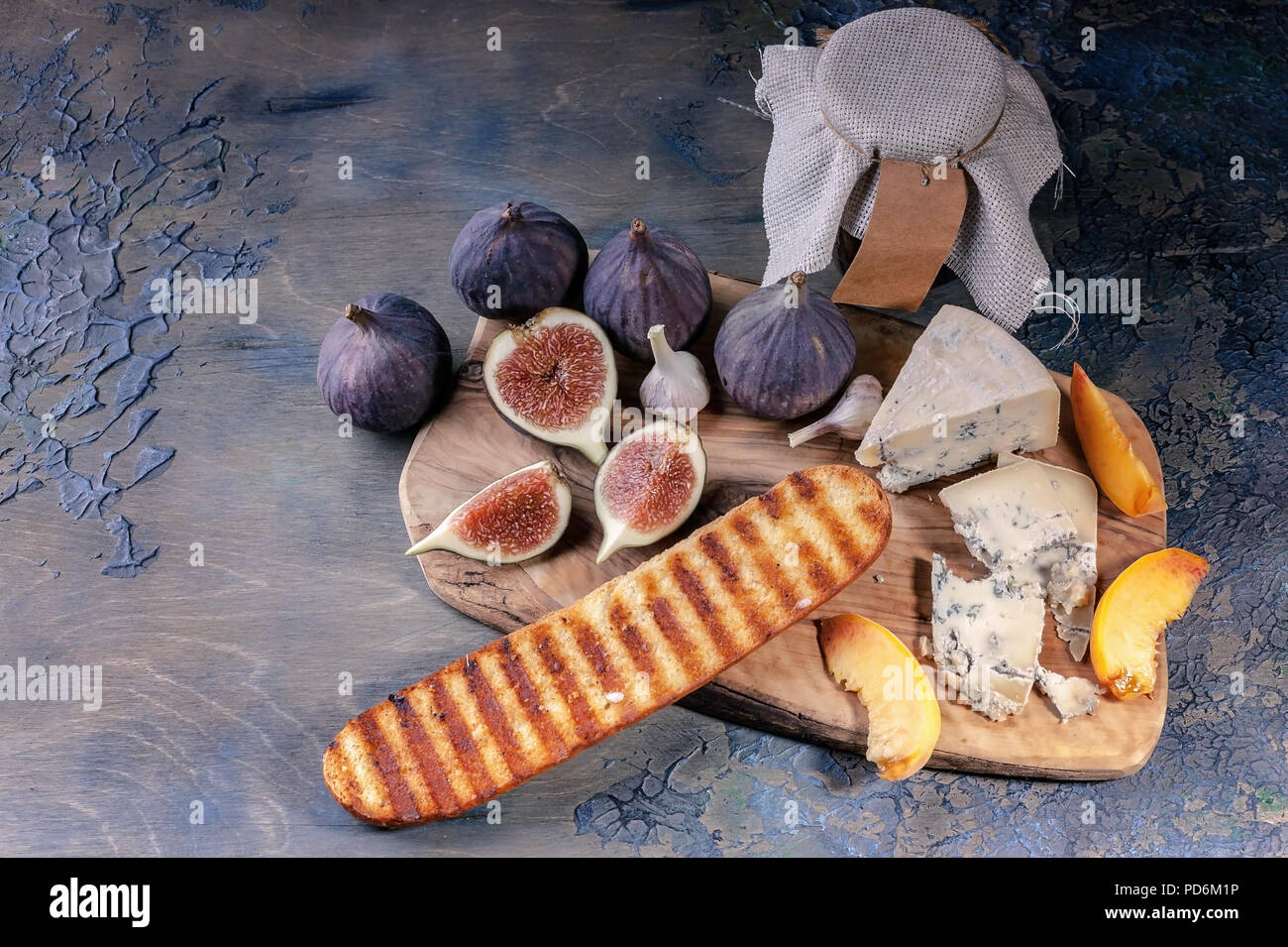 Fichi maturi, nobile formaggio con stampo, fette di pesche e baguette su un tagliere. Foto Stock