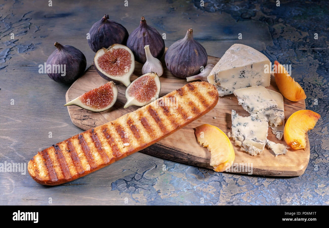 Fichi maturi, nobile formaggio con stampo, fette di pesche e baguette su un tagliere. Foto Stock