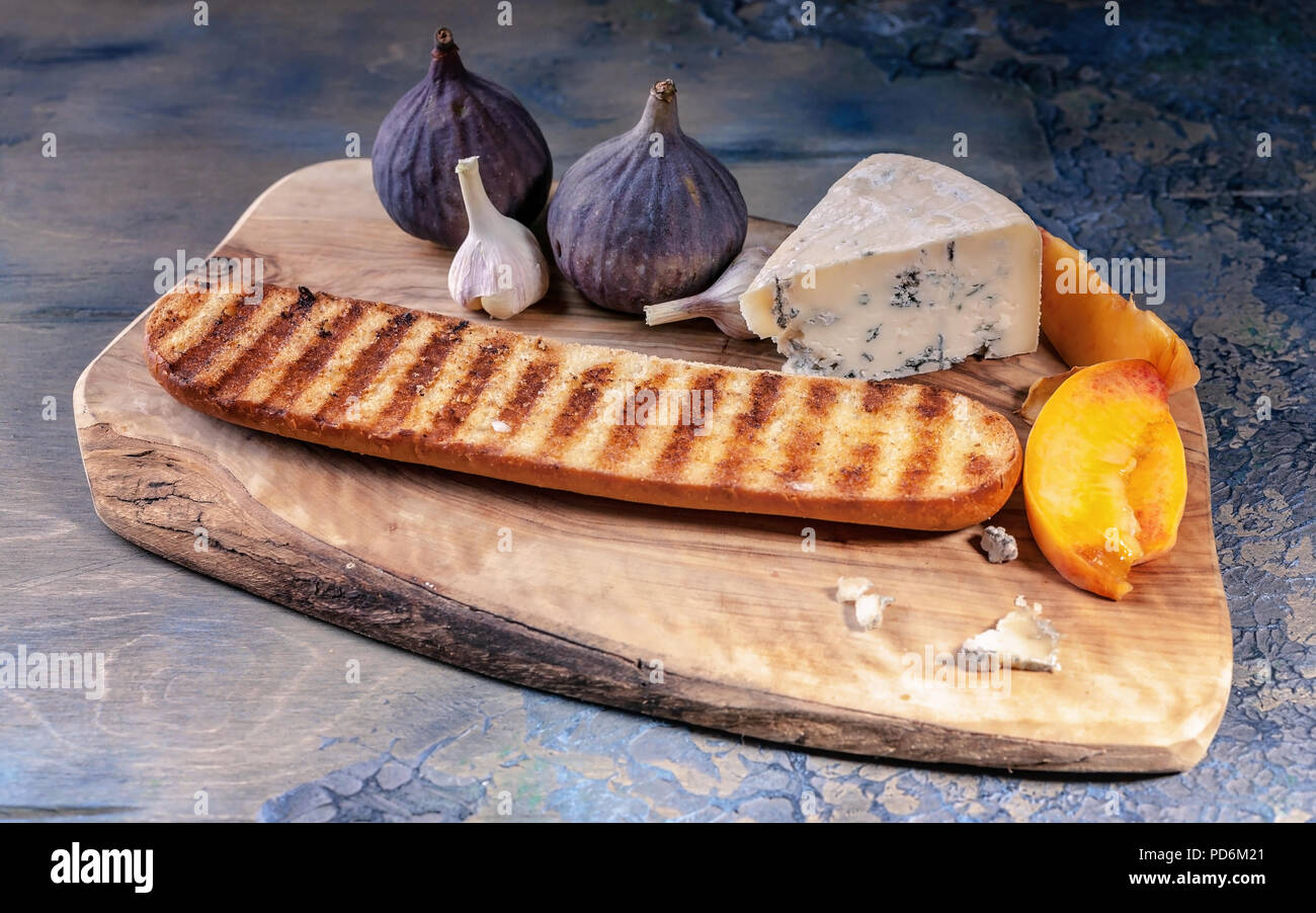 Fichi maturi, nobile formaggio con stampo, fette di pesche e baguette su un tagliere. Foto Stock