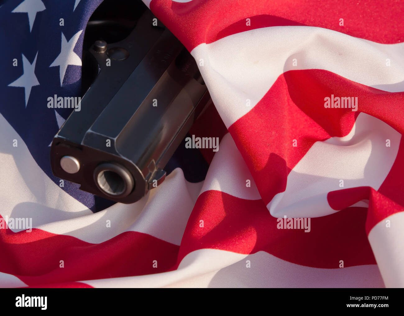 Una pistola nera la museruola sporgenti avvolti in una bandiera americana Foto Stock