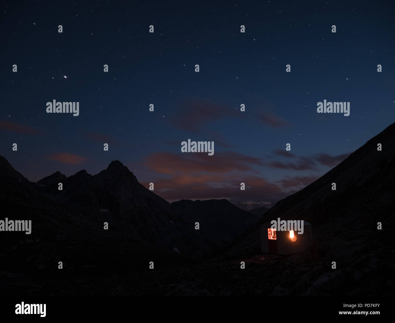 La Via Lattea e il cielo stellato dall'alto sulle Alpi con scenic paesaggio di montagna. Persone in piedi da parte una piccola cappella con un fulmine sulla marcia Foto Stock