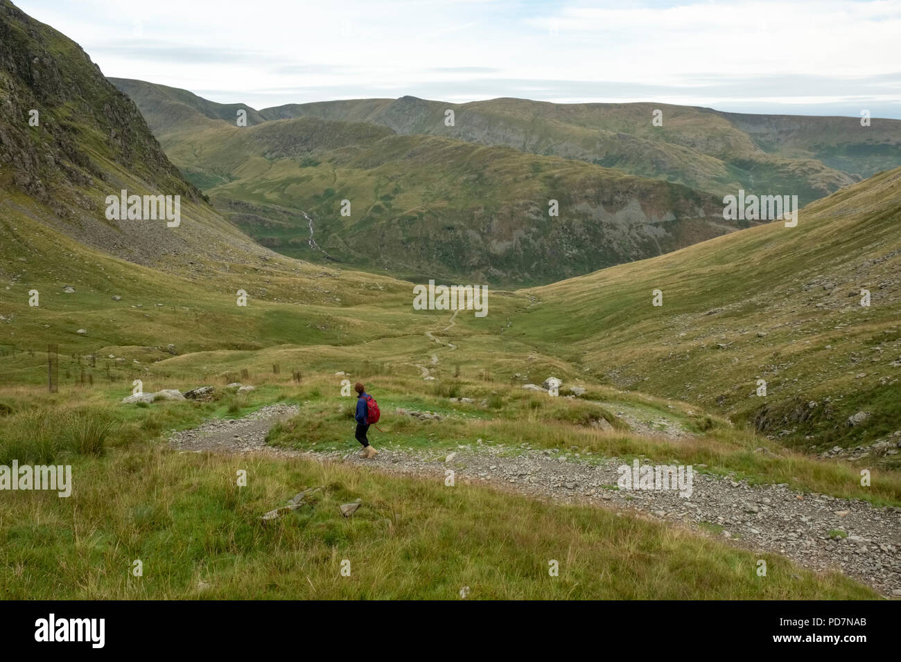 Donna con zaino camminando verso il basso di un roccioso passo di montagna circondato da colline e montagne nel distretto del lago, Cumbria Foto Stock