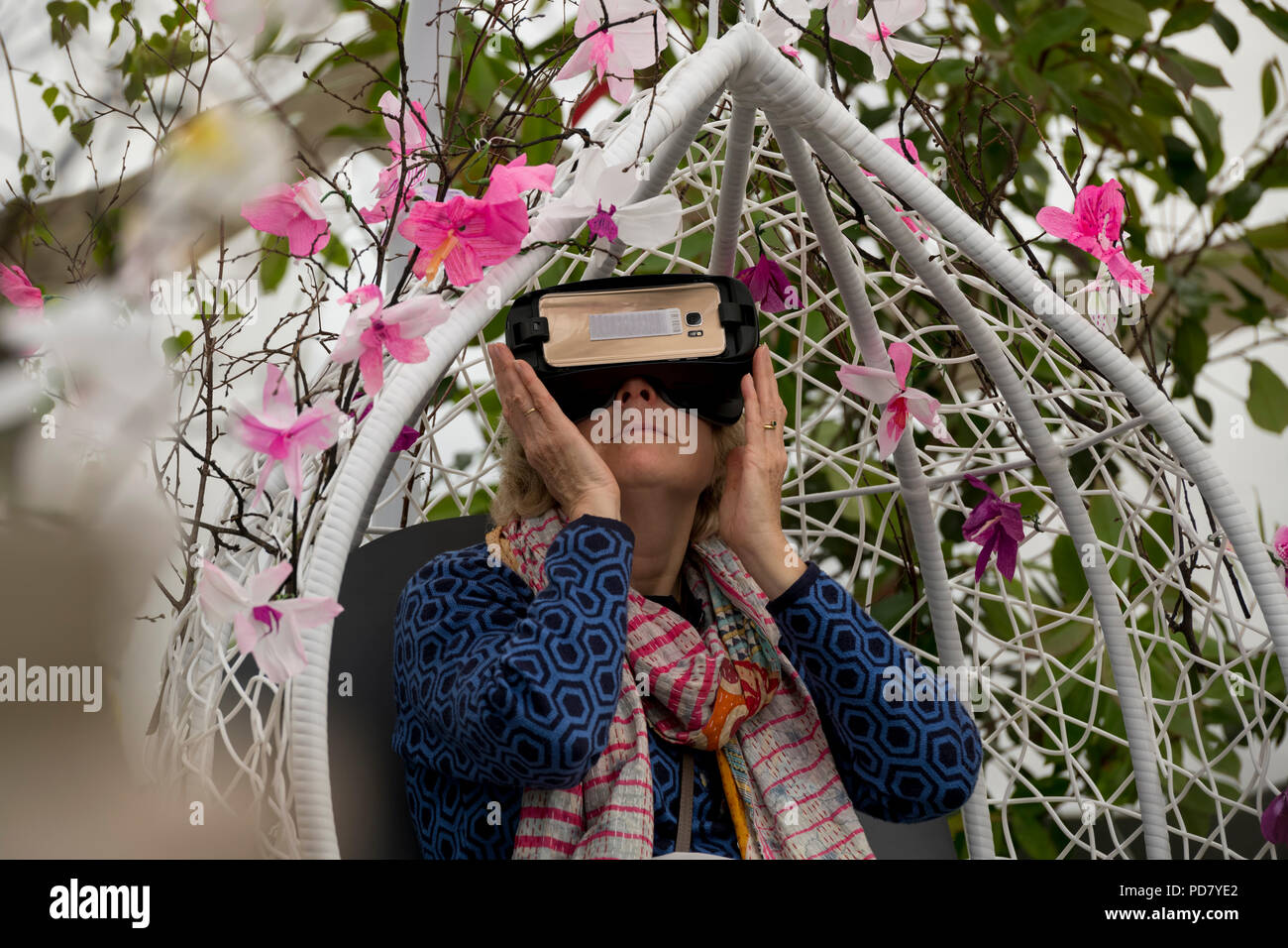 Donna che indossa le cuffie VR, seduto al posto di guida tra i fiori in realtà virtuale esperienza di orchidee - RHS Chatsworth Flower Show, Derbyshire, Inghilterra, Regno Unito. Foto Stock