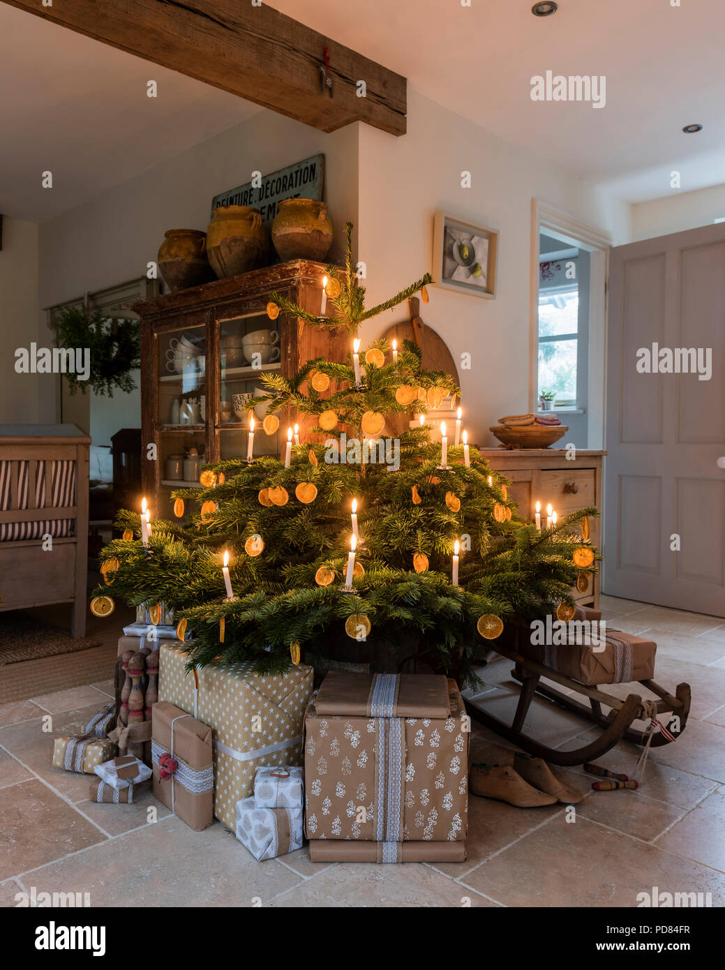 Candela albero di Natale illuminato in cottage cucina con soffitto con travi in legno a vista e regali impacchettati Foto Stock