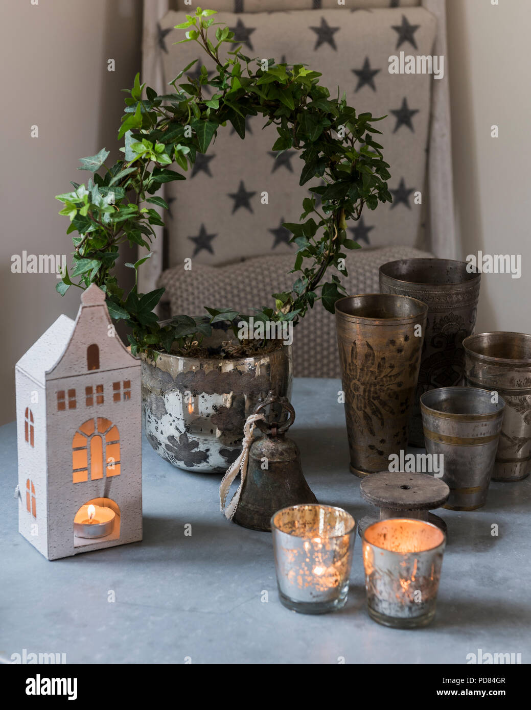 Selezione delle tealight e piccola ghirlanda di edera sul piano del tavolo con coppe in peltro Foto Stock