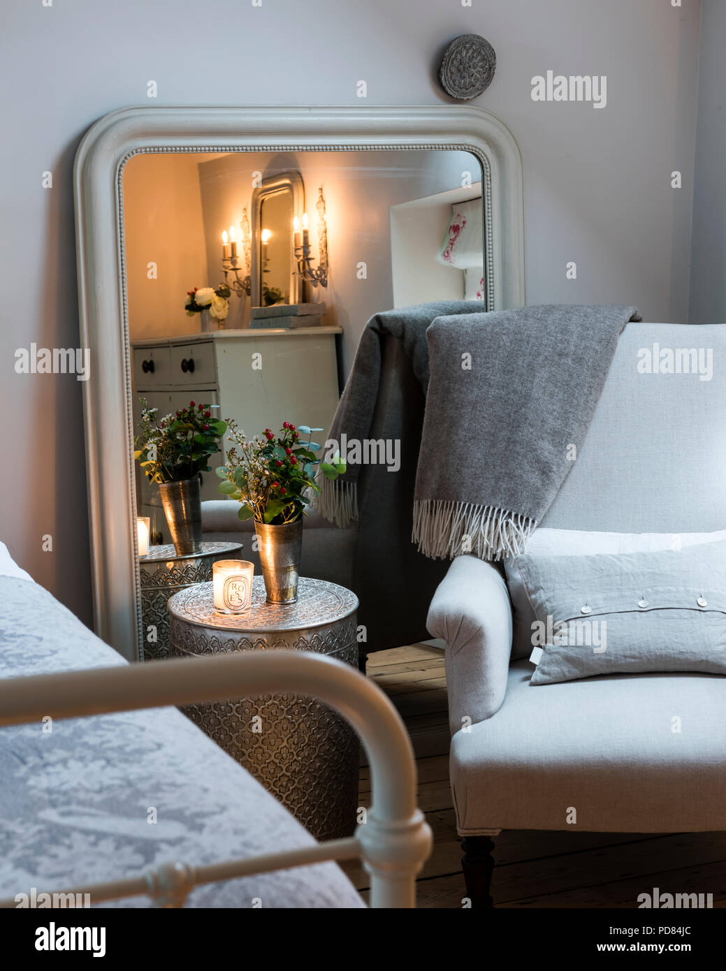 Poltrona e coperta di lana buttare in camera da letto angolo con un grande specchio, fiori freschi e candele Foto Stock