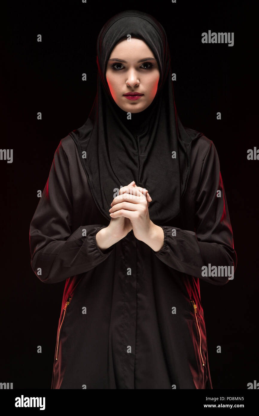 Ritratto di bella gravi giovani musulmani donna vestita di nero hijab con la mano sulla mano come pregare concetto su sfondo nero Foto Stock