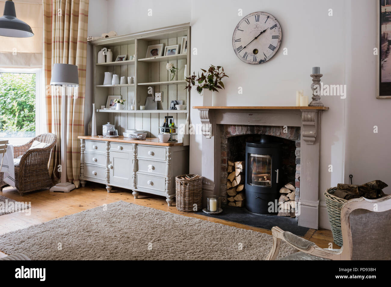 Grande comò in accogliente piano aperto sala colazione con orologio da parete, woodburning stufa e sedie di vimini Foto Stock